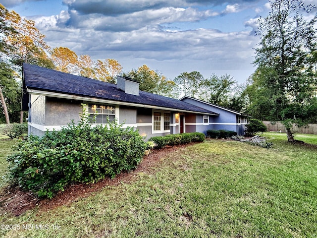 rear view of house featuring a lawn, a chimney, and stucco siding