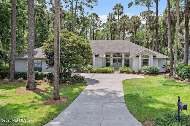 view of front of home featuring a front lawn, stucco siding, concrete driveway, a shingled roof, and view of wooded area