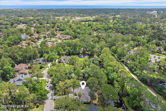 aerial view of property and surrounding area featuring a heavily wooded area and nearby suburban area