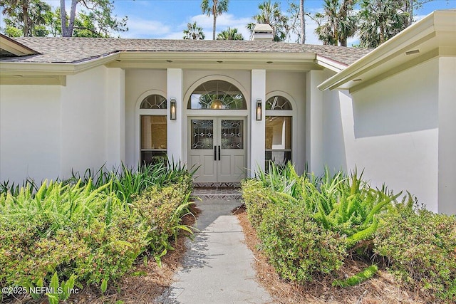 property entrance with a shingled roof, stucco siding, and a chimney