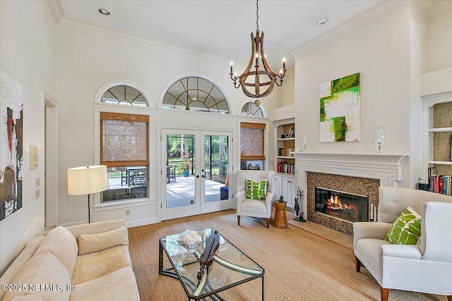 living area featuring crown molding, built in features, a premium fireplace, french doors, and a chandelier