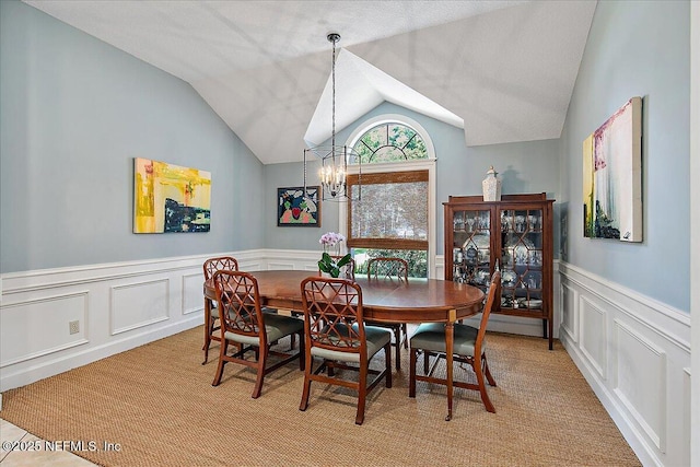 dining space with a chandelier, lofted ceiling, a decorative wall, a wainscoted wall, and light colored carpet