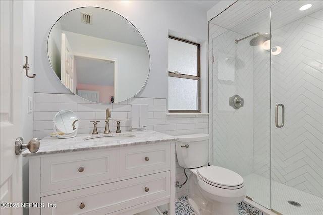 full bathroom with a shower stall, tile walls, toilet, and vanity