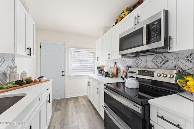 kitchen with tasteful backsplash, appliances with stainless steel finishes, light countertops, light wood-style floors, and white cabinetry