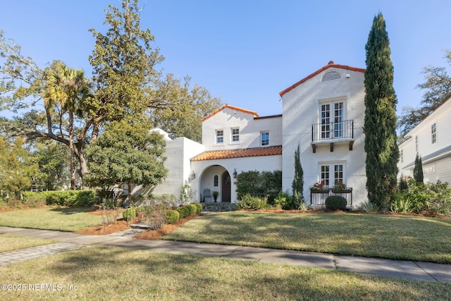 mediterranean / spanish house with french doors, a front yard, and a balcony