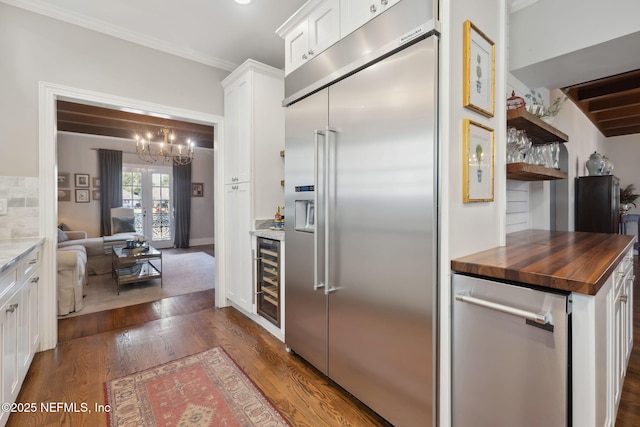 kitchen with appliances with stainless steel finishes, wooden counters, dark wood-type flooring, white cabinets, and ornamental molding