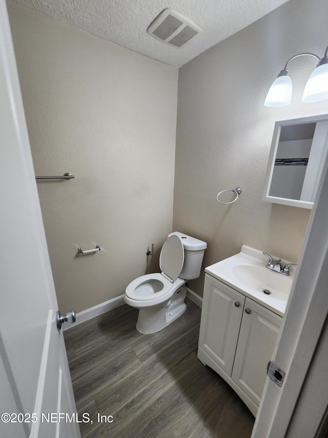 bathroom with visible vents, toilet, vanity, a textured ceiling, and wood finished floors