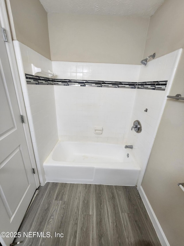 bathroom with a textured ceiling, bathtub / shower combination, baseboards, and wood finished floors