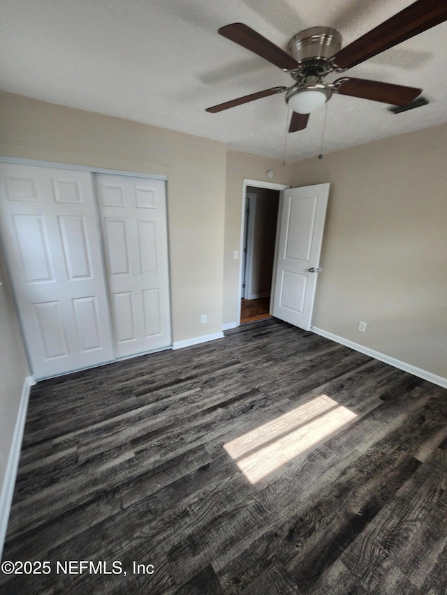 unfurnished bedroom featuring ceiling fan, visible vents, baseboards, a closet, and dark wood finished floors