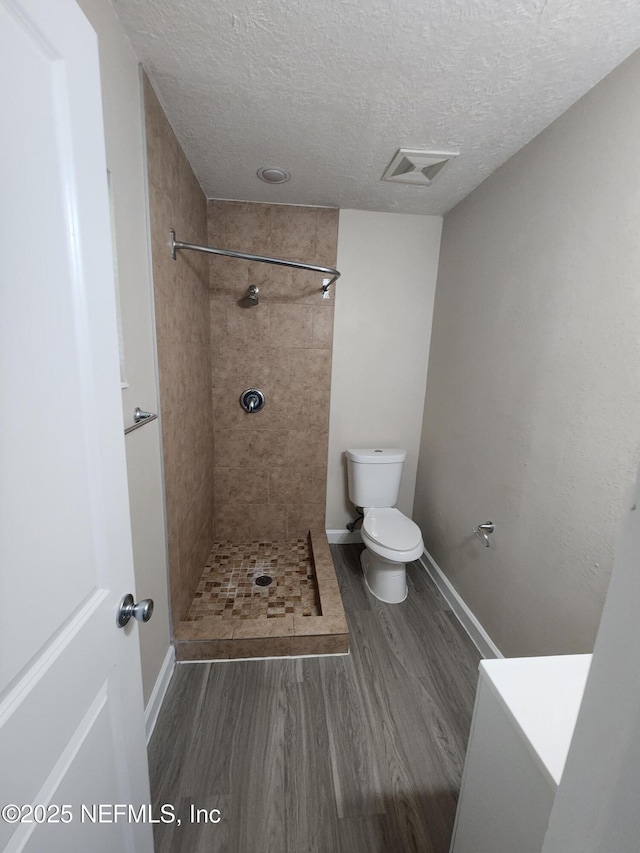 full bathroom with visible vents, tiled shower, toilet, wood finished floors, and a textured ceiling