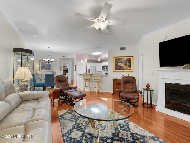 4306 Serena Cir, Saint Augustine, FL 32084 - living room featuring ceiling fan with notable chandelier, ornamental molding, a glass covered fireplace, visible vents, and wood finished floors