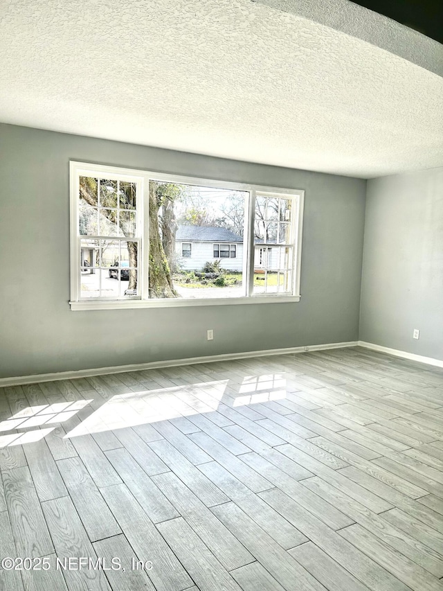 unfurnished room featuring light wood finished floors, a wealth of natural light, and baseboards