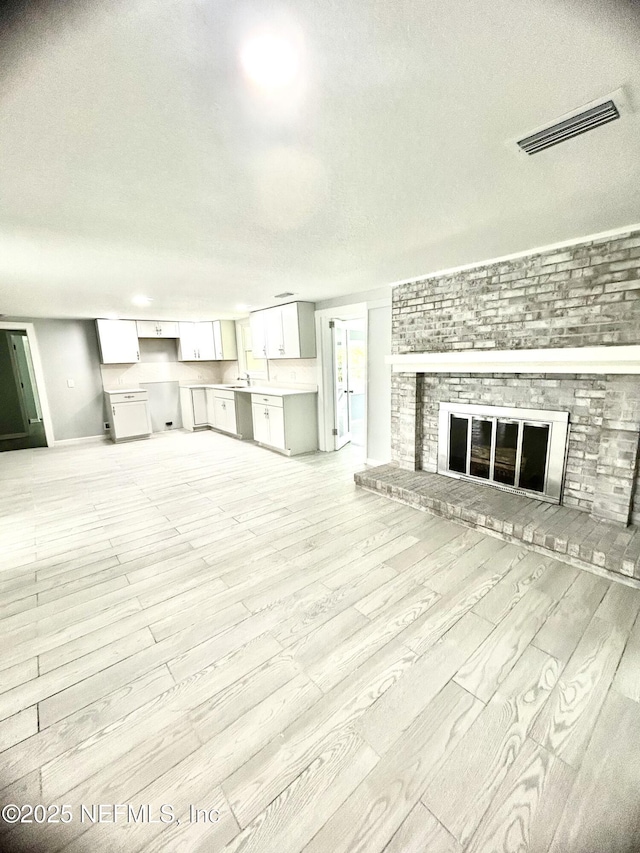 unfurnished living room featuring light wood-style floors, a brick fireplace, visible vents, and a textured ceiling