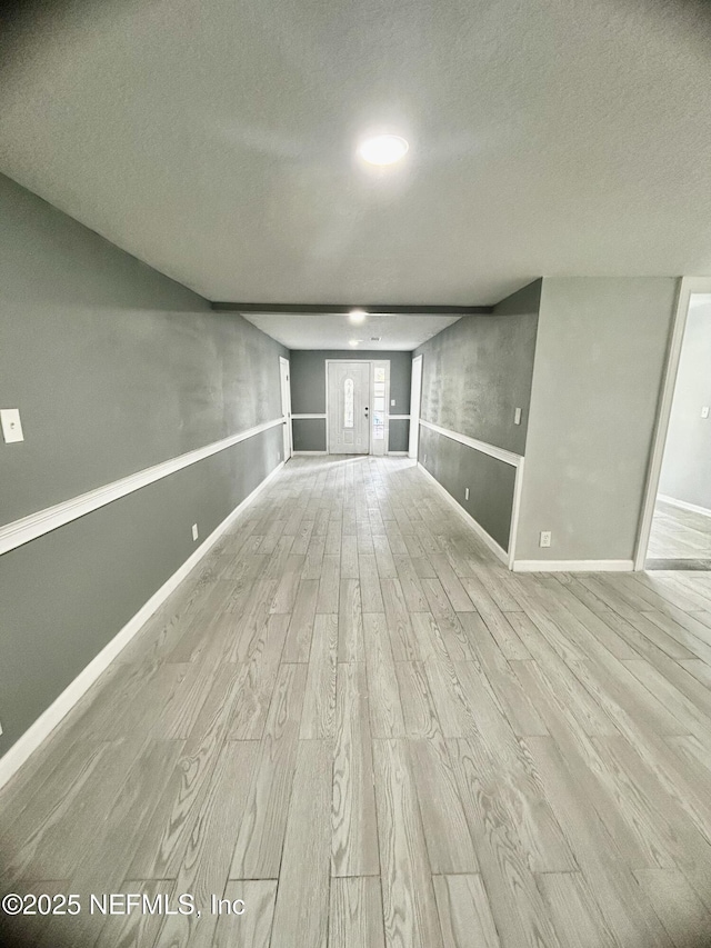 unfurnished living room featuring light wood-type flooring, baseboards, and a textured ceiling