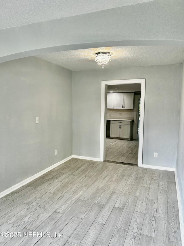 unfurnished room with light wood-style flooring, baseboards, and a textured ceiling