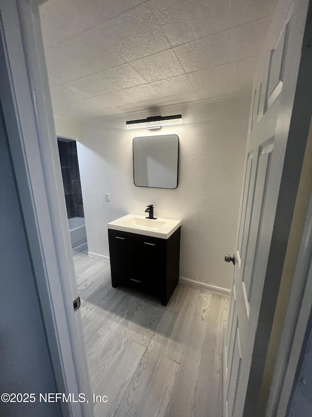 bathroom featuring a textured wall, a drop ceiling, wood finished floors, vanity, and baseboards