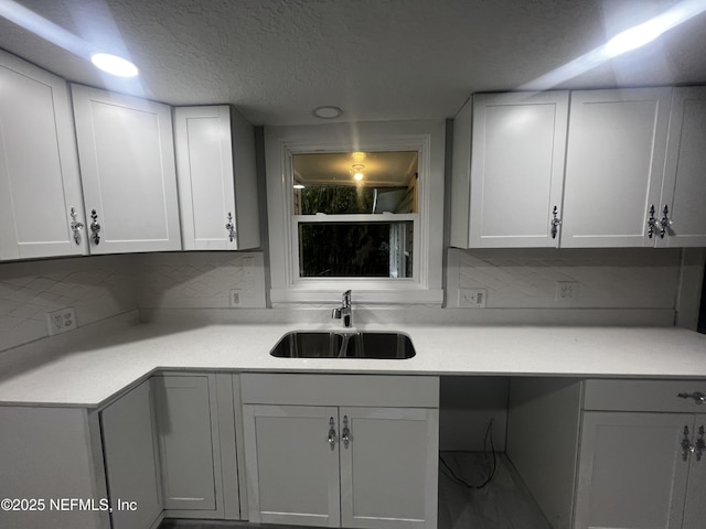 kitchen with white cabinets, light countertops, a sink, and decorative backsplash