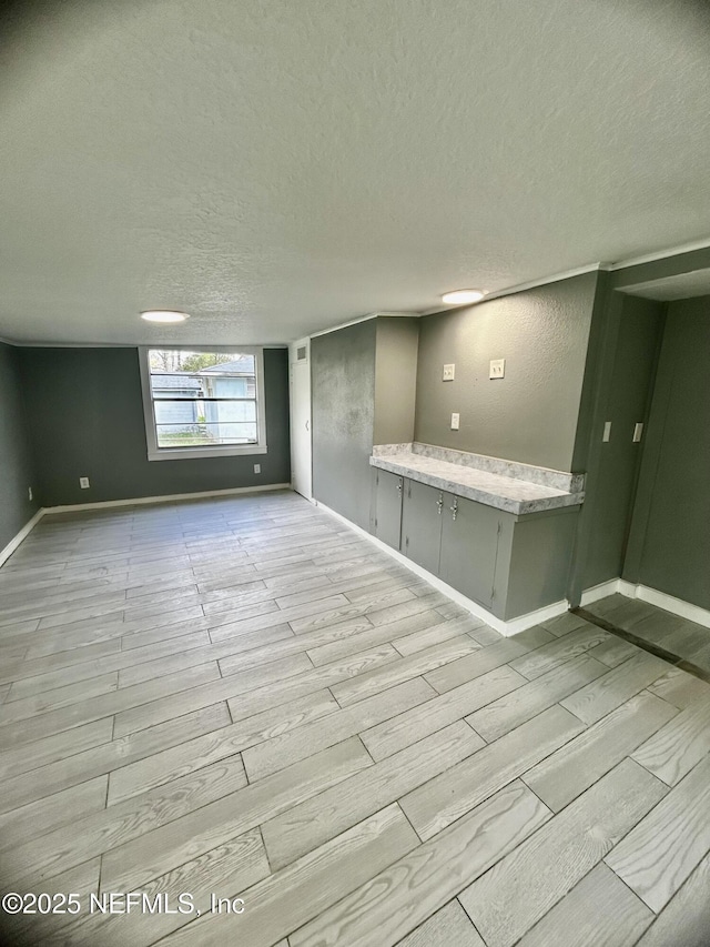 unfurnished room featuring light wood-style flooring, a textured ceiling, and baseboards