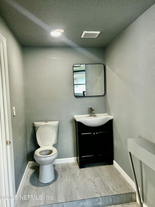 half bathroom featuring a textured ceiling, toilet, vanity, visible vents, and wood tiled floor