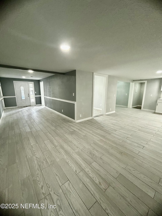 below grade area featuring a textured ceiling, light wood-style flooring, and baseboards