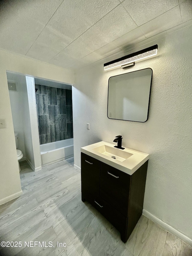 bathroom with toilet, washtub / shower combination, baseboards, and vanity