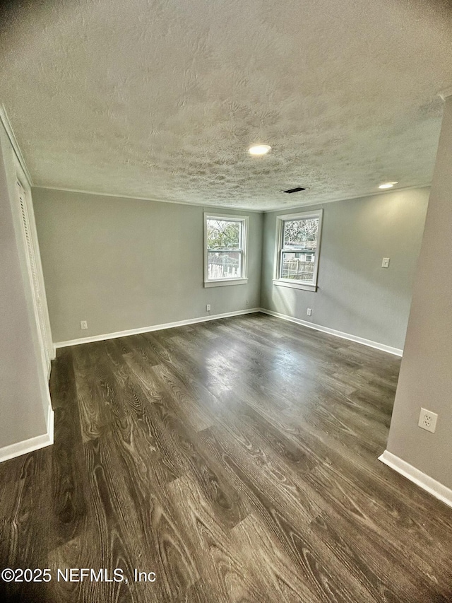 spare room featuring dark wood-type flooring, a textured ceiling, and baseboards