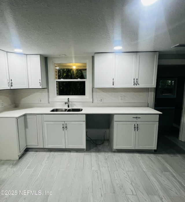 kitchen featuring a sink, light countertops, a textured ceiling, light wood-style floors, and backsplash