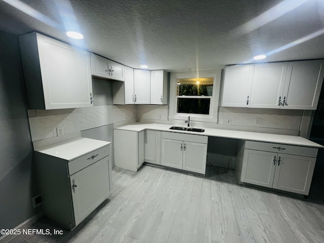 kitchen featuring tasteful backsplash, light wood-style flooring, light countertops, a textured ceiling, and a sink