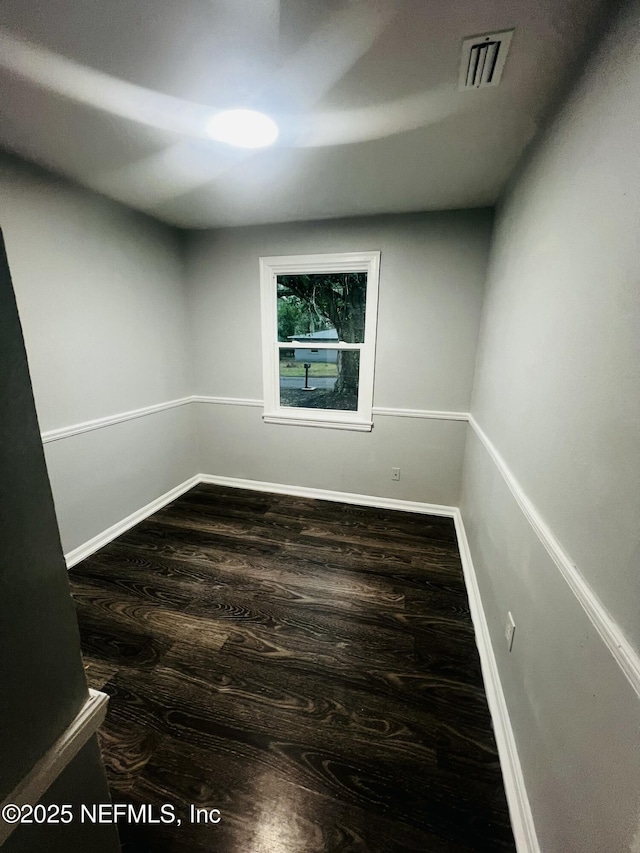 empty room featuring dark wood-style flooring, visible vents, and baseboards