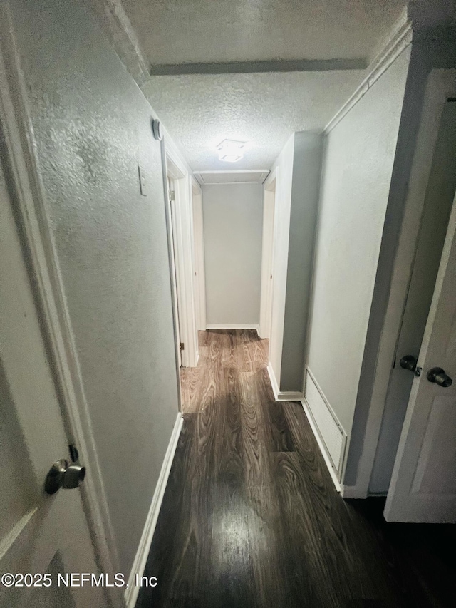 corridor featuring dark wood-type flooring, a textured ceiling, and baseboards