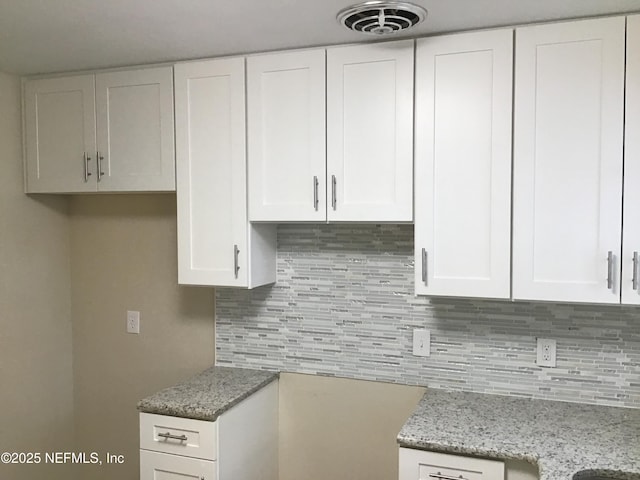 kitchen with white cabinetry, backsplash, visible vents, and light stone countertops