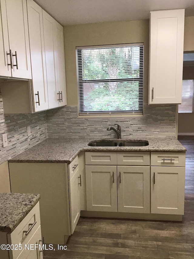 kitchen with backsplash, a sink, light stone countertops, and white cabinets