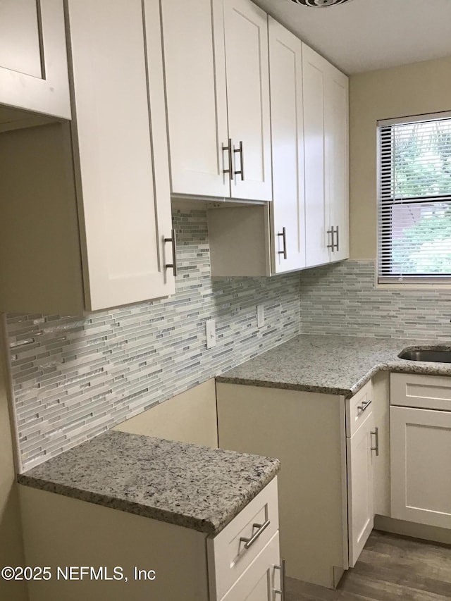 kitchen with dark wood-style flooring, decorative backsplash, white cabinetry, a sink, and light stone countertops