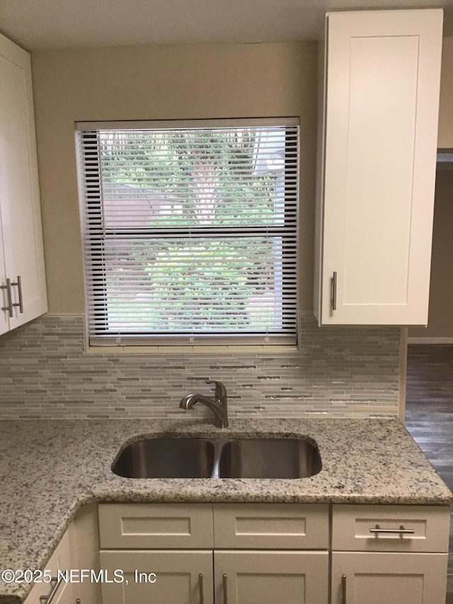 kitchen with light stone countertops, white cabinetry, backsplash, and a sink