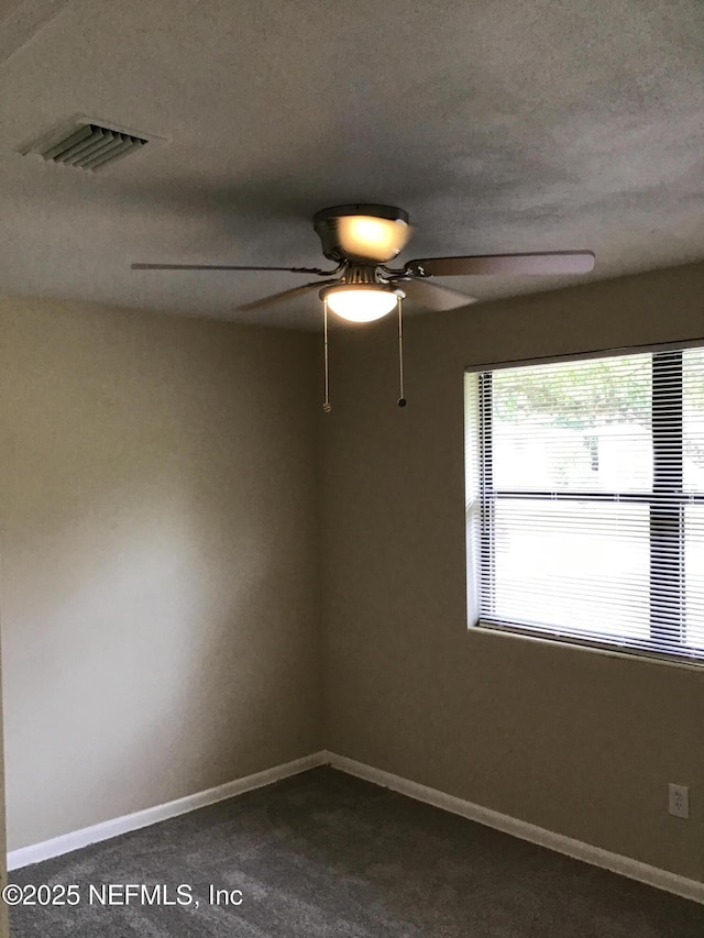 spare room with visible vents, dark carpet, a textured ceiling, and baseboards