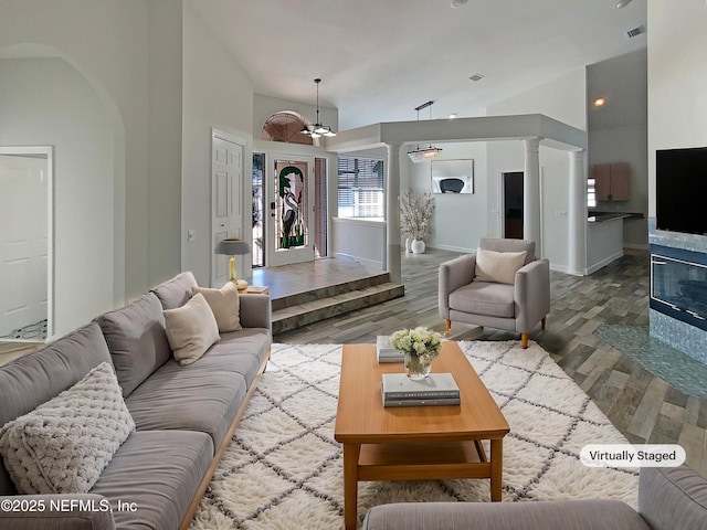 living room with baseboards, visible vents, wood finished floors, ornate columns, and high vaulted ceiling