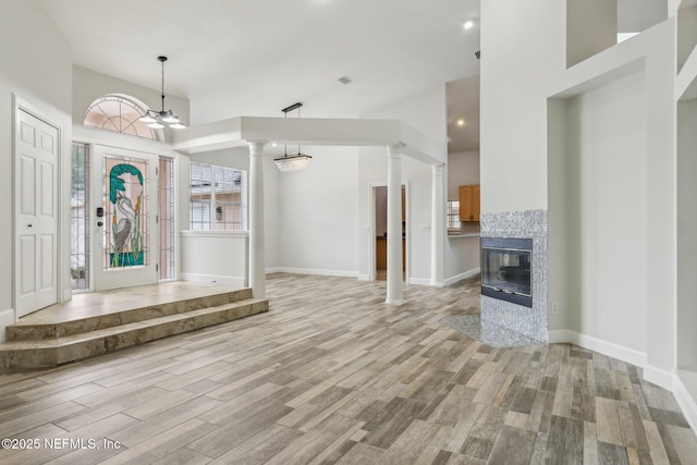 foyer entrance with a chandelier, a tiled fireplace, light wood-style flooring, and ornate columns