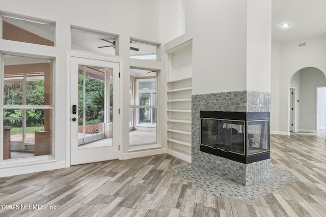 unfurnished living room with built in shelves, a fireplace, wood finished floors, a towering ceiling, and visible vents