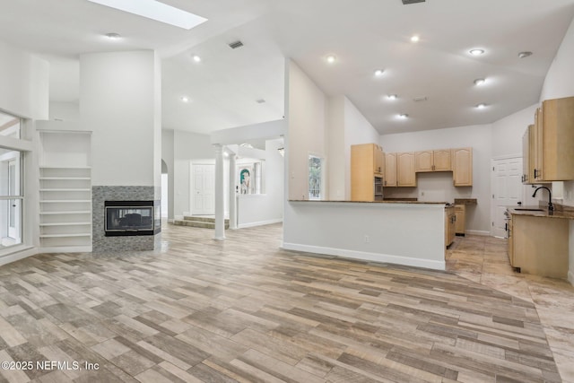 kitchen featuring visible vents, a tile fireplace, open floor plan, light brown cabinets, and a sink