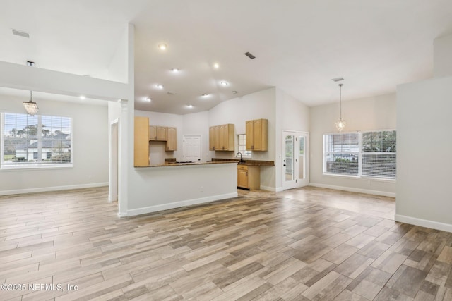 kitchen featuring dark countertops, open floor plan, light brown cabinetry, light wood-style floors, and pendant lighting