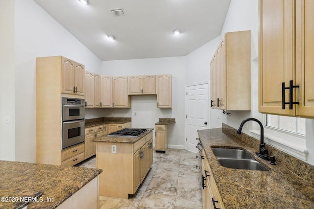 kitchen featuring a sink, appliances with stainless steel finishes, a center island, light brown cabinetry, and dark stone countertops