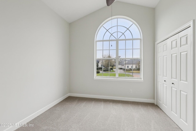 carpeted empty room with vaulted ceiling and baseboards