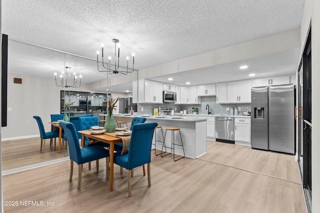 dining space with sink, light wood-type flooring, an inviting chandelier, and a textured ceiling