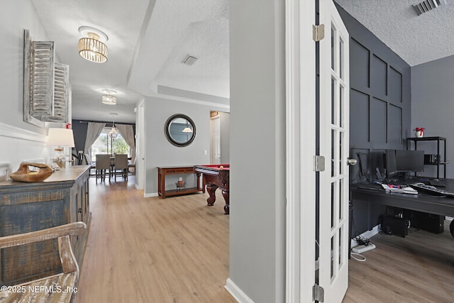 hall with a textured ceiling, light wood-style flooring, visible vents, and baseboards