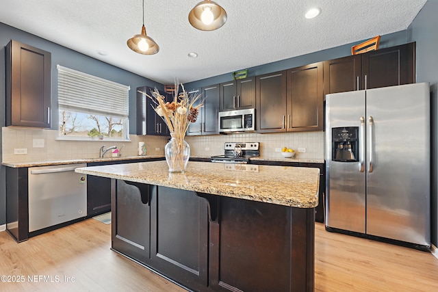 kitchen featuring appliances with stainless steel finishes, light wood-style floors, decorative light fixtures, and a center island