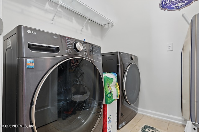 clothes washing area featuring laundry area, light tile patterned flooring, washing machine and dryer, and baseboards