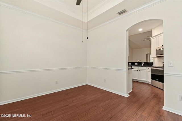 unfurnished dining area featuring dark wood-type flooring, ceiling fan, a raised ceiling, ornamental molding, and sink