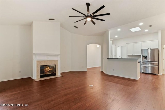 unfurnished living room with ceiling fan, a tiled fireplace, and dark wood-type flooring