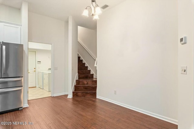 interior space with stainless steel refrigerator, separate washer and dryer, white cabinetry, wood-type flooring, and a chandelier