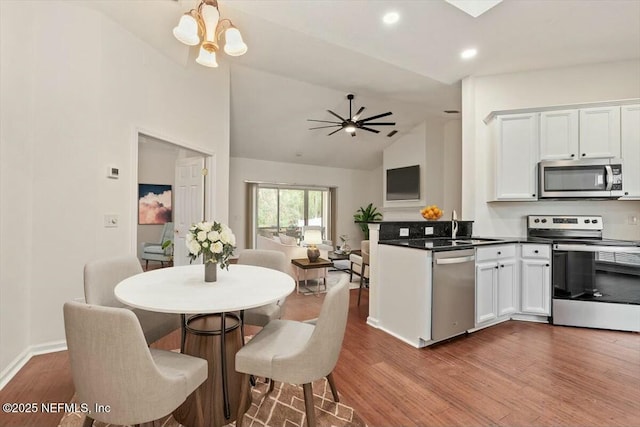 kitchen featuring appliances with stainless steel finishes, hardwood / wood-style floors, kitchen peninsula, ceiling fan with notable chandelier, and white cabinets